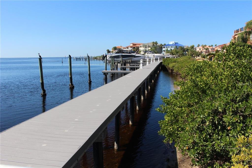 A long wooden dock extends over the water toward houses and boats along the shore — 4557 HARBORPOINTE DRIVE, PORT RICHEY, FL