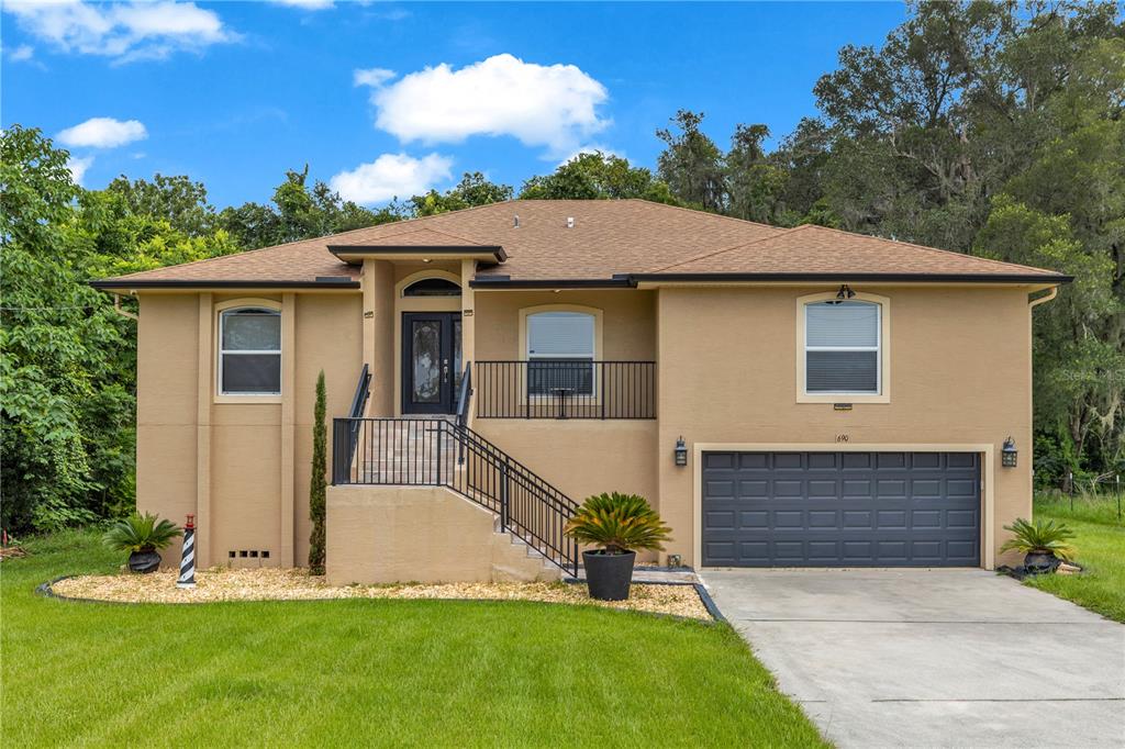 A tan, elevated two-story house with a front staircase, dark garage door, and landscaped yard — 690 W LISBON PARKWAY, DELAND, FL