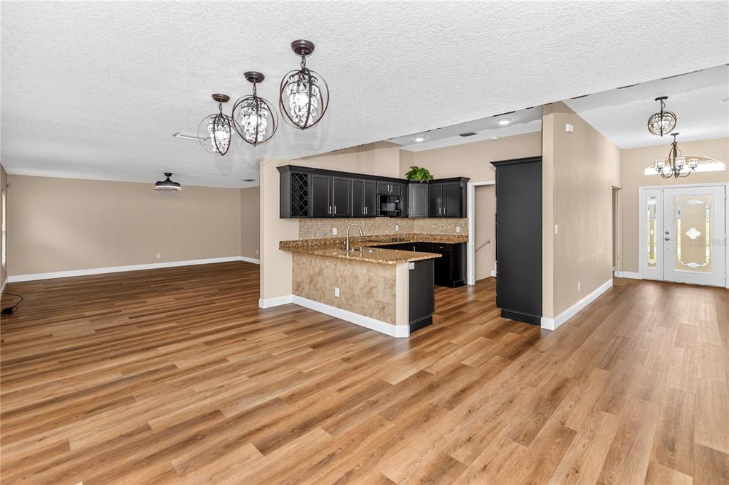 An open-concept kitchen with dark cabinets and granite countertops overlooks a spacious living area — 690 W LISBON PARKWAY, DELAND, FL