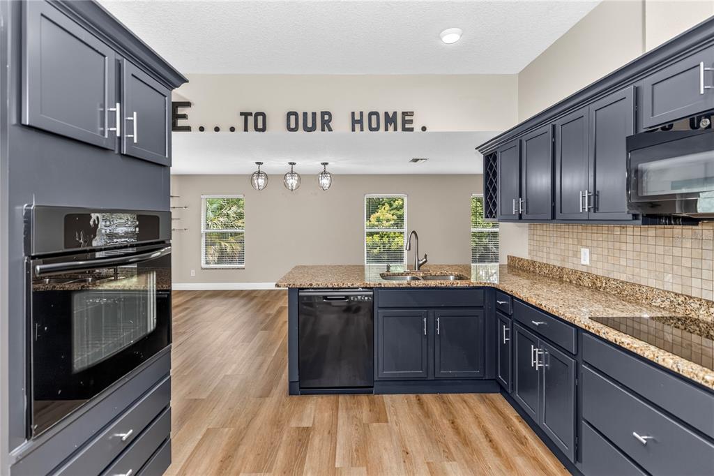 A kitchen with dark blue cabinets, granite countertops, and wood-look flooring opens to a living area — 690 W LISBON PARKWAY, DELAND, FL