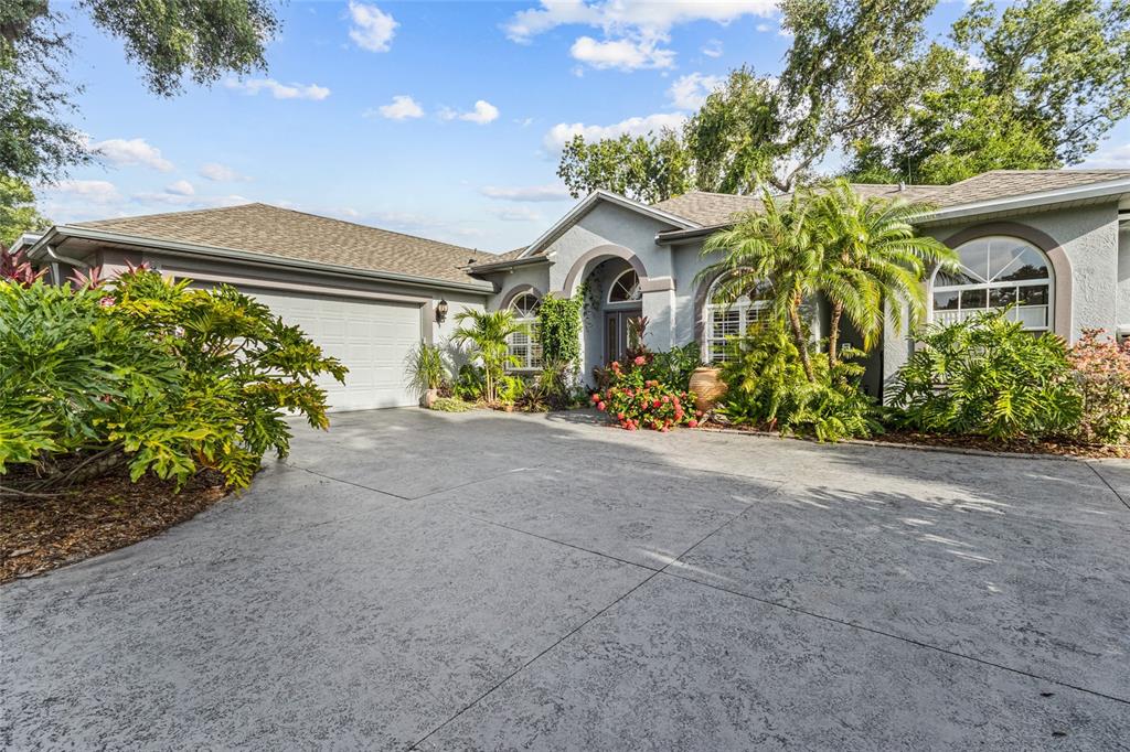 A single-story house with a gray stucco exterior, a concrete driveway, and lush landscaping — 3025 RIVER WOODS DRIVE, PARRISH, FL