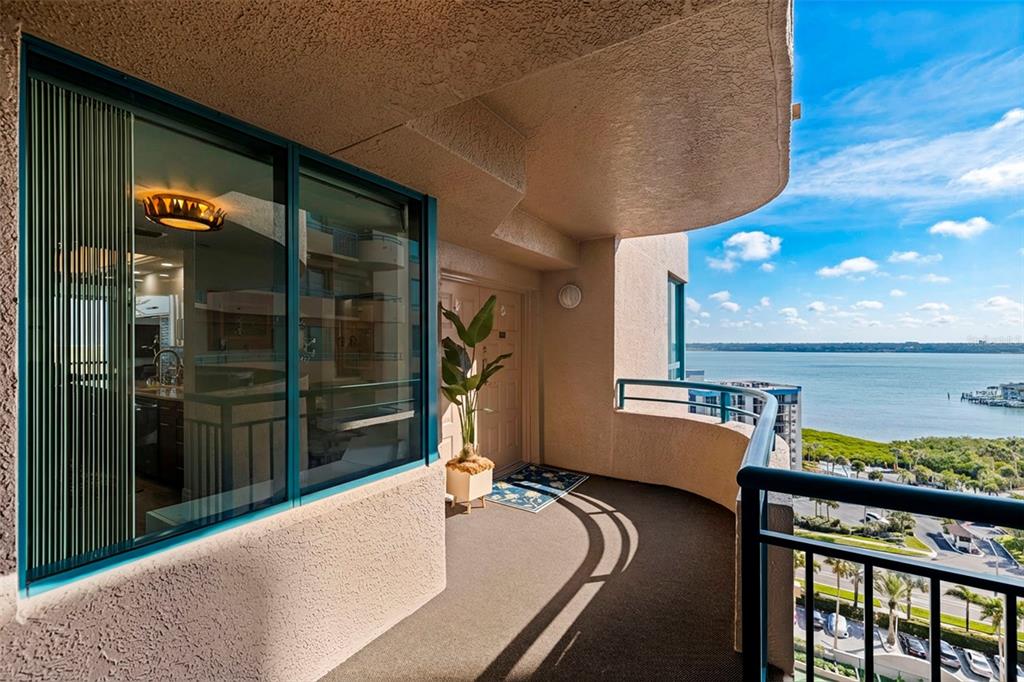 A curved balcony with dark carpeting overlooks a body of water and a parking lot — 1520 GULF BOULEVARD UNIT 1506, CLEARWATER BEACH, FL