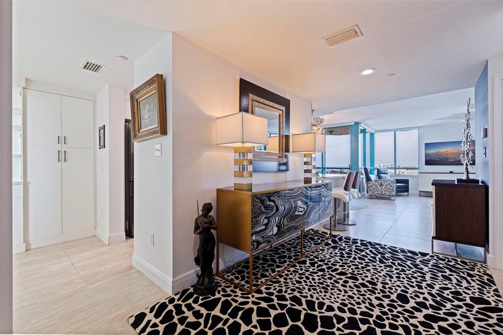 A foyer with a patterned rug, a gold-accented console table, and lamps leads to a living area — 1520 GULF BOULEVARD UNIT 1506, CLEARWATER BEACH, FL