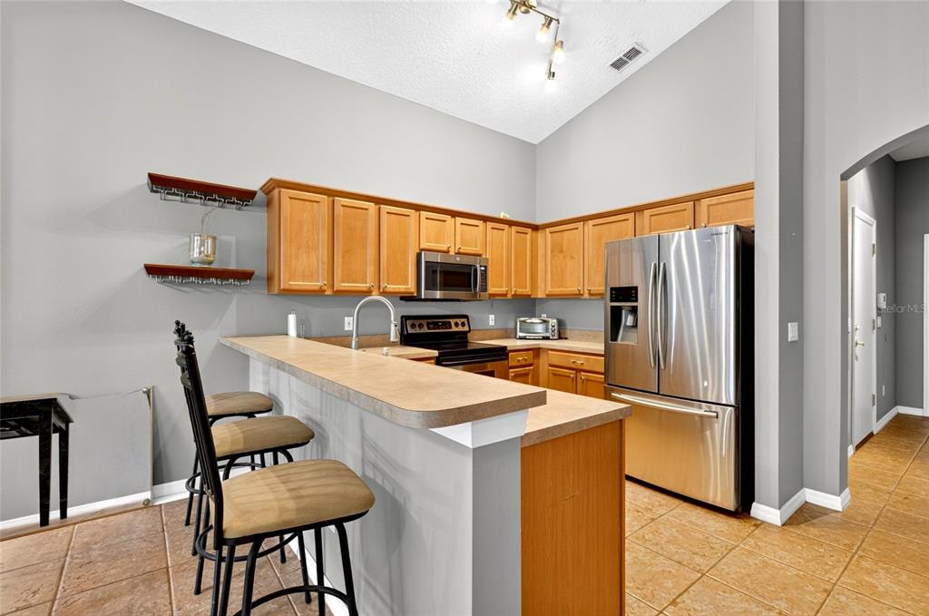 A kitchen features wood cabinets, stainless steel appliances, a breakfast bar, and tile flooring — 4618 CONROY CLUB DRIVE, ORLANDO, FL