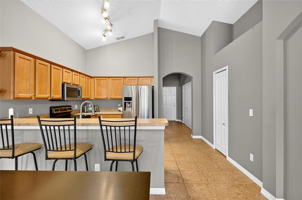 A kitchen features light wood cabinets, stainless steel appliances, a breakfast bar, and tile flooring — 4618 CONROY CLUB DRIVE, ORLANDO, FL
