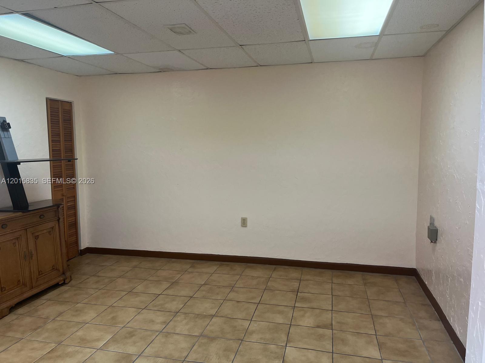 An empty room features beige walls, brown tile flooring, a drop ceiling, and a wooden cabinet — 1545 SW 1st St, Miami FL 33135, MIAMI, FL