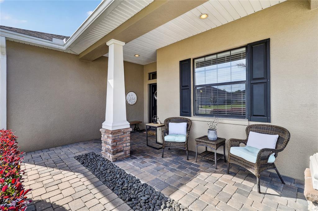 A covered front porch features paver flooring, a stone-based pillar, and two wicker chairs — 4427 MICANOPE CRESCENT DRIVE, LAKELAND, FL