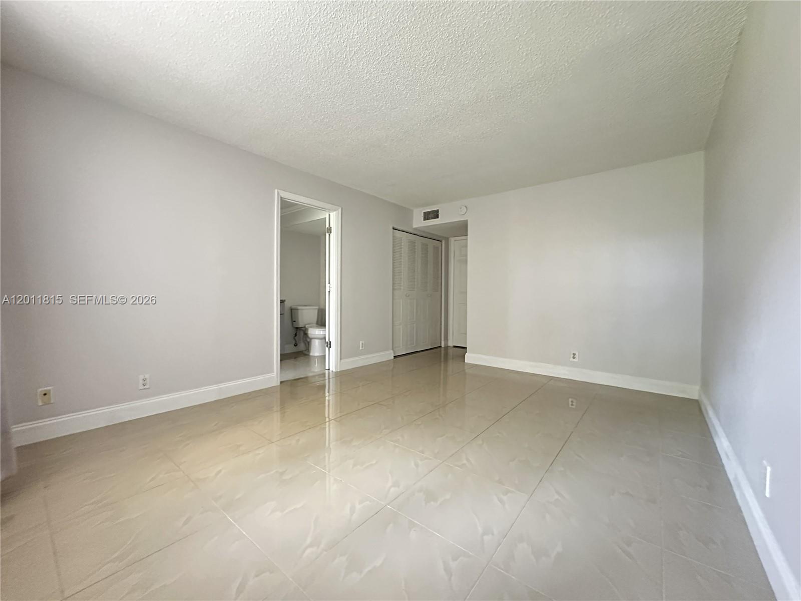 An empty room features light-colored tile flooring, gray walls, and a doorway leading to a bathroom — 9370 SW 8th St # 107, Boca Raton FL 33428, BOCA RATON, FL