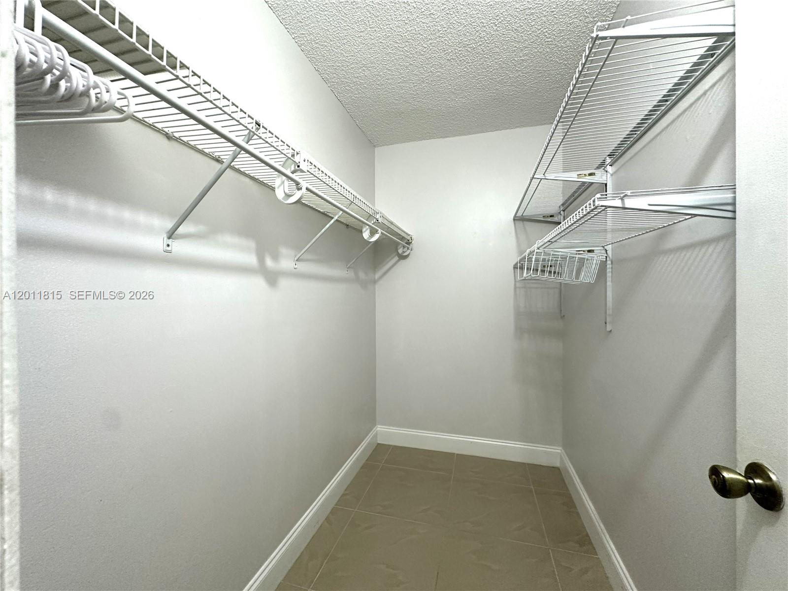A walk-in closet features white wire shelving, light-colored walls, and tiled flooring — 9370 SW 8th St # 107, Boca Raton FL 33428, BOCA RATON, FL