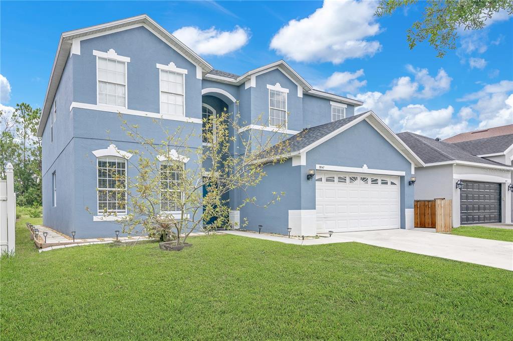 A two-story blue house with a white garage and a front yard under a sky — 5047 ADAIR OAK DRIVE, ORLANDO, FL