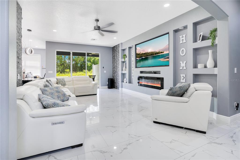 A living room features white leather furniture, marble-look tile floors, and a built-in fireplace wall — 5047 ADAIR OAK DRIVE, ORLANDO, FL