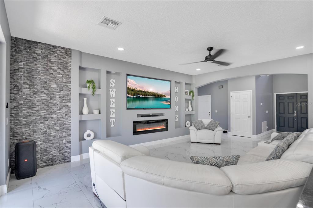 A living room features a stone accent wall, built-in shelving, a fireplace, and white furniture — 5047 ADAIR OAK DRIVE, ORLANDO, FL