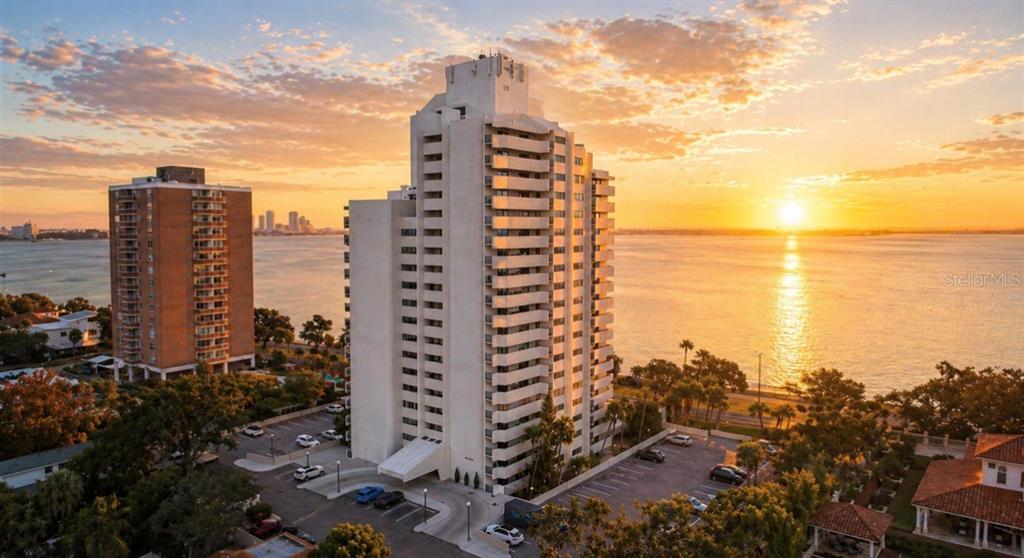An aerial view of a tall white residential building at sunset beside a large body of water — 4141 BAYSHORE BOULEVARD UNIT 606, TAMPA, FL
