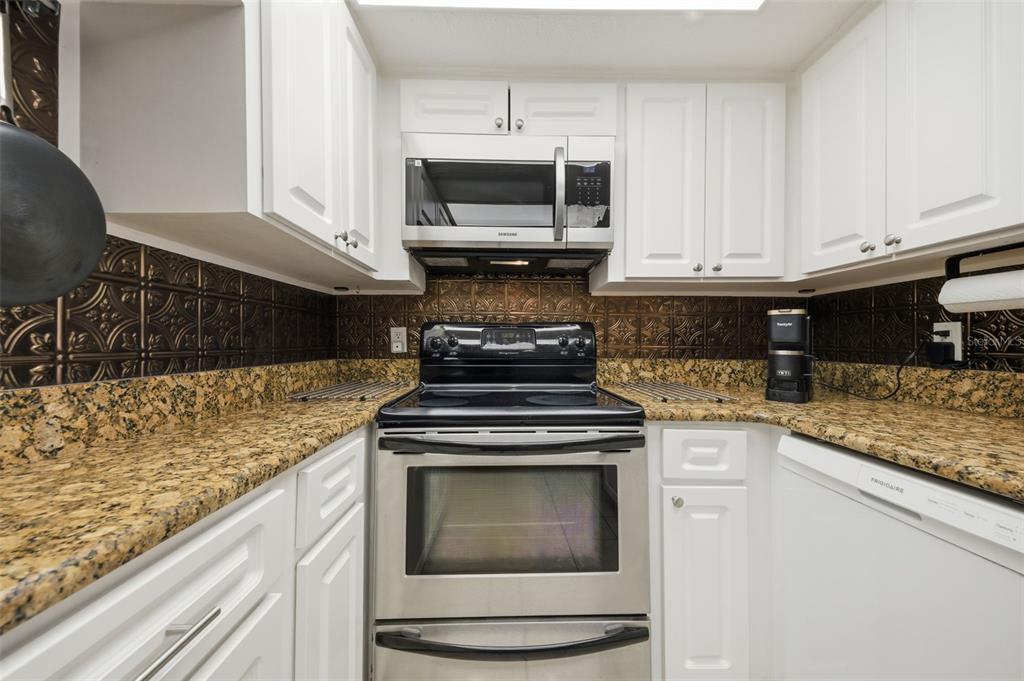 A kitchen features white cabinets, granite countertops, a stainless steel stove, and a metallic backsplash — 4141 BAYSHORE BOULEVARD UNIT 606, TAMPA, FL