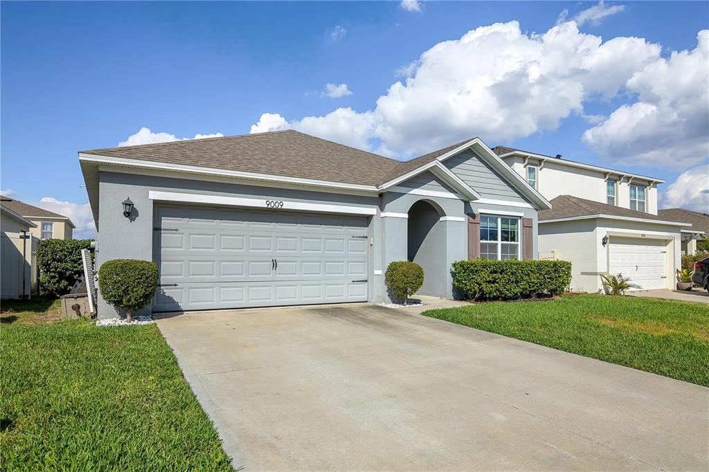 A single-story suburban house features a gray exterior, a two-car garage, and a concrete driveway — 9009 PINALES WAY, KISSIMMEE, FL