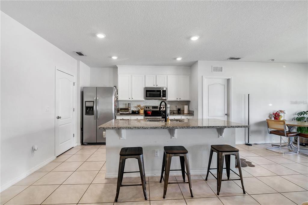A kitchen features white cabinets, granite countertops, a center island with stools, and tile flooring — 9009 PINALES WAY, KISSIMMEE, FL