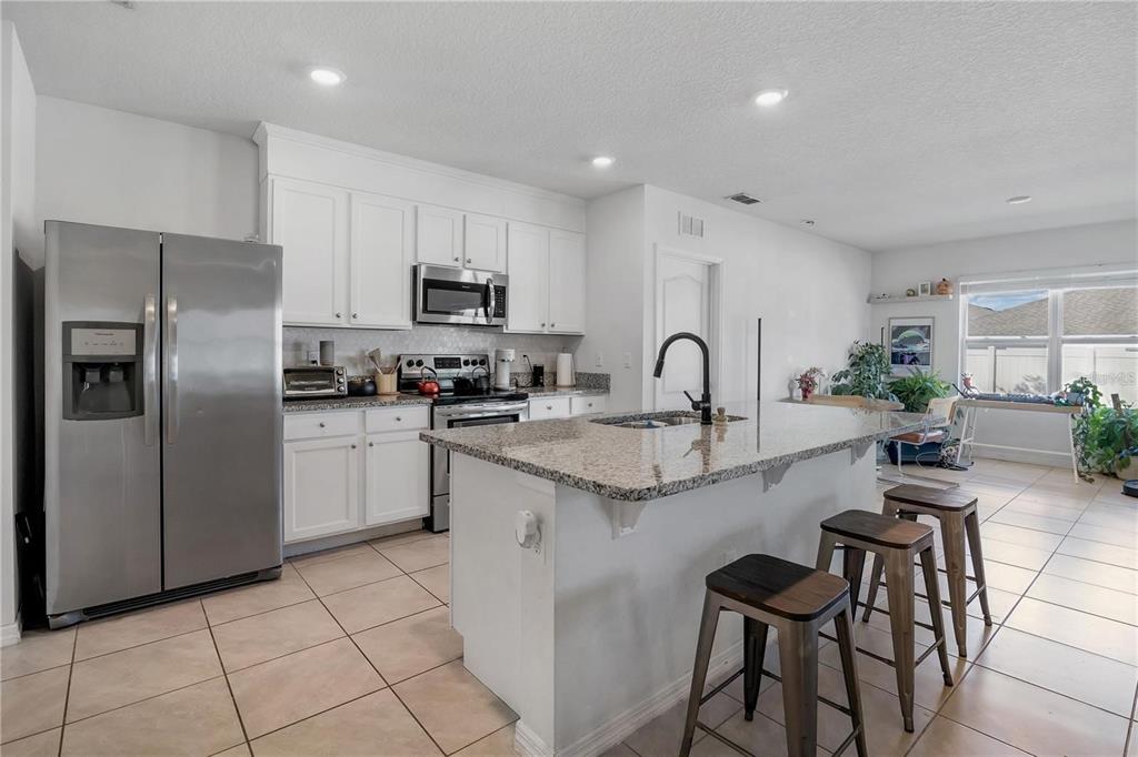 A kitchen with white cabinets, stainless steel appliances, a granite island, and tile flooring — 9009 PINALES WAY, KISSIMMEE, FL