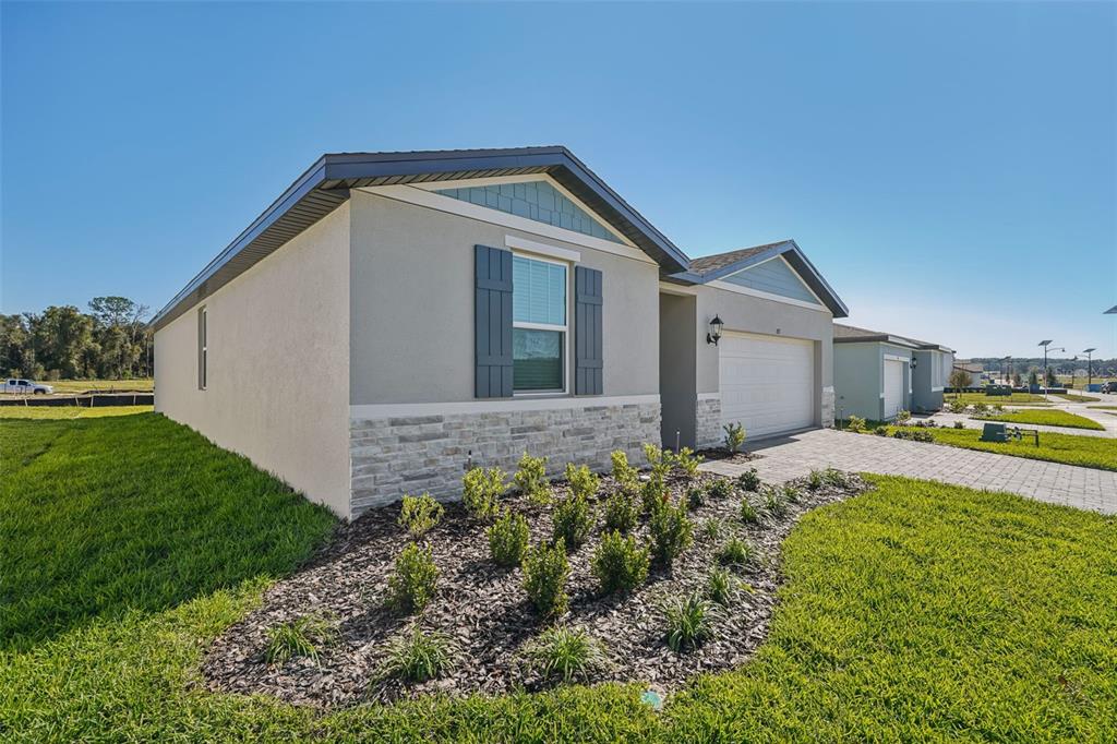 A single-story suburban house features a stone facade, gray stucco walls, and a paved driveway — 851 SUNSHOWER DRIVE, LADY LAKE, FL