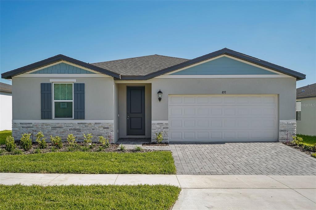 A single-story house with a gray stucco exterior, stone accents, and a two-car garage — 851 SUNSHOWER DRIVE, LADY LAKE, FL