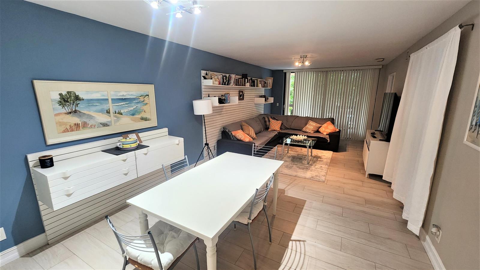A living and dining area features blue walls, wood-look tile flooring, and a slat wall — 600 Egret Circle # 7201, Delray Beach FL 33444, DELRAY BEACH, FL