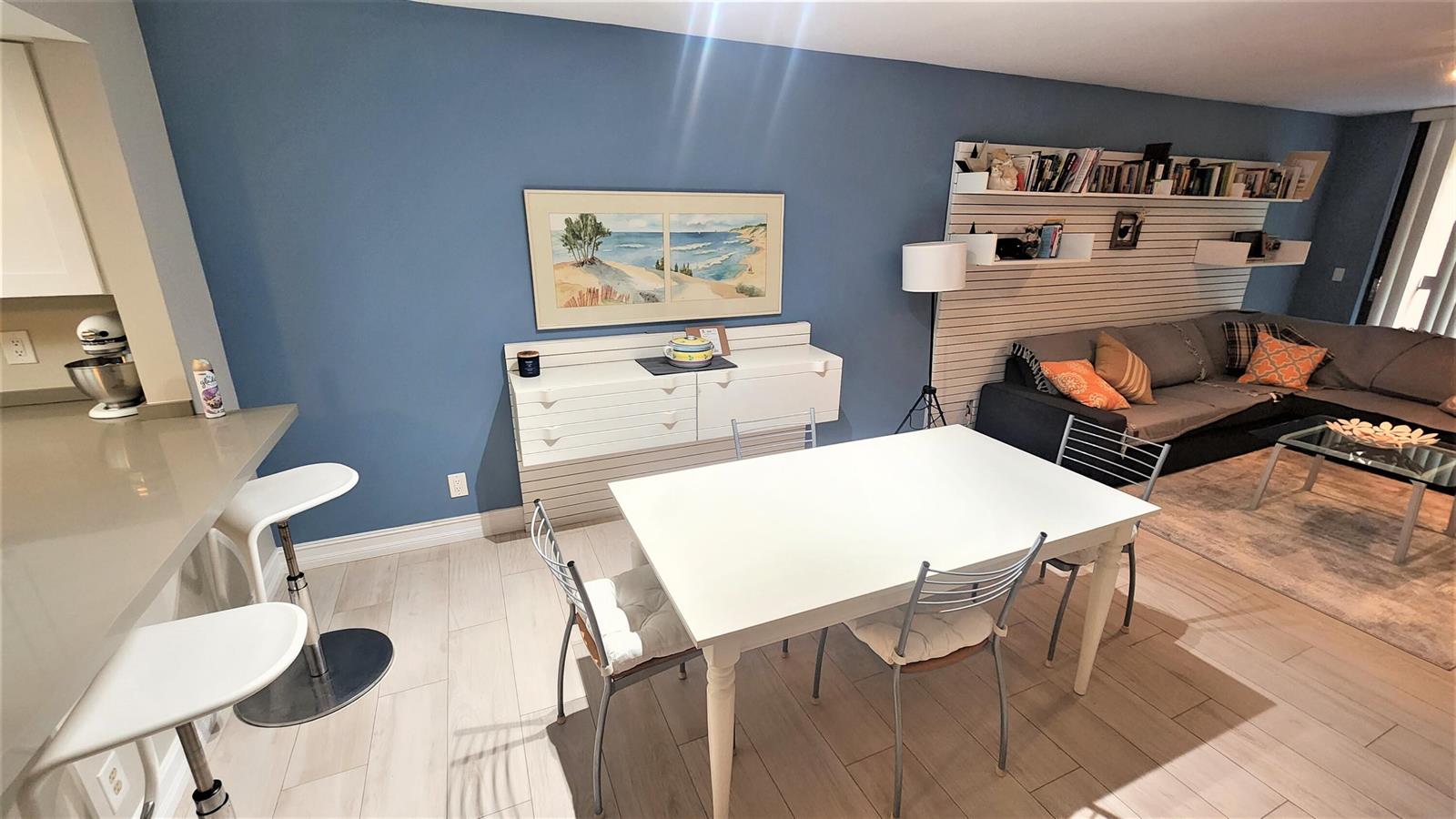 A dining area with a white table and chairs sits next to a blue-walled living room — 600 Egret Circle # 7201, Delray Beach FL 33444, DELRAY BEACH, FL