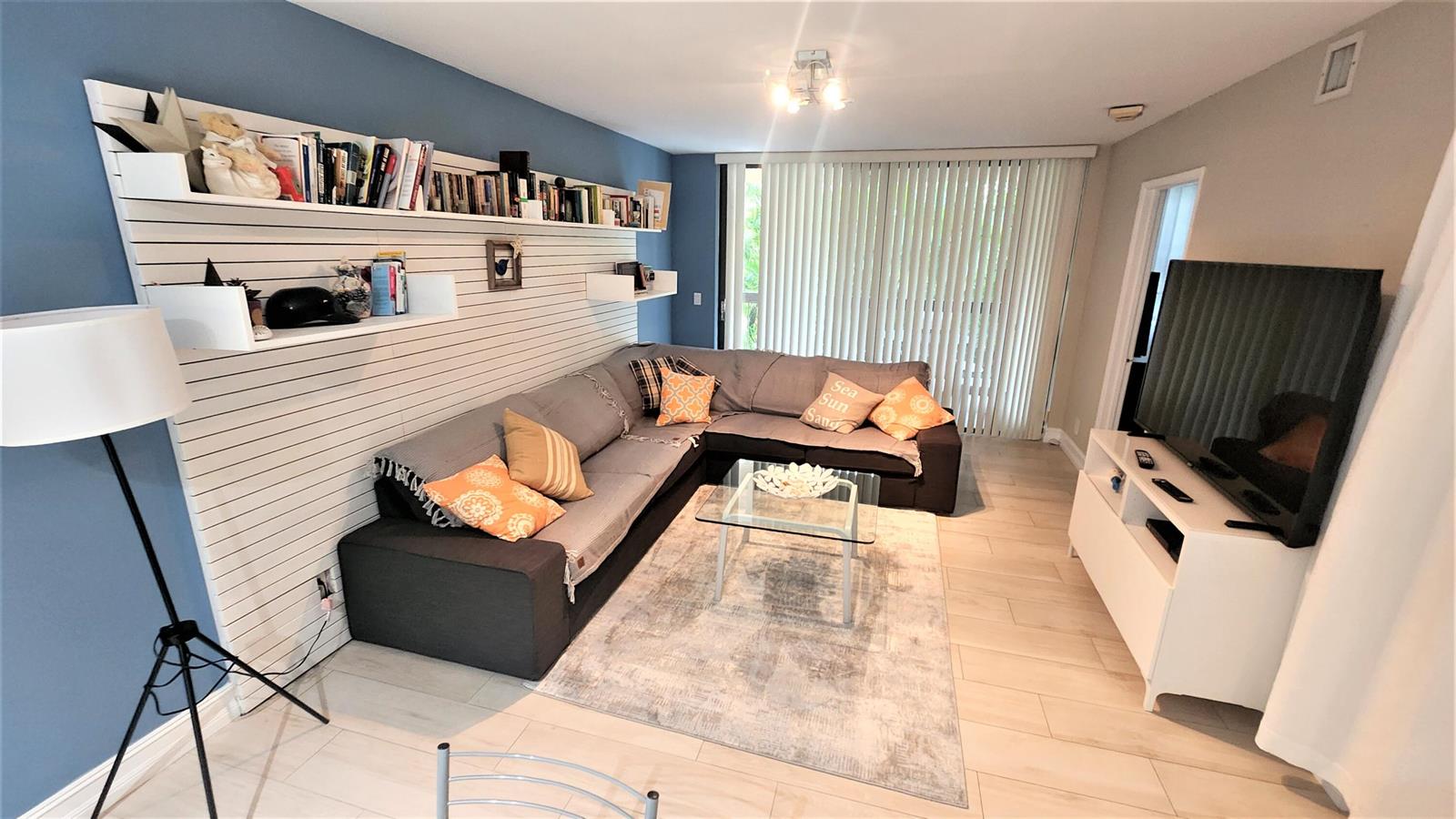 A living room features a grey sectional sofa, a glass coffee table, and slat-wall shelving — 600 Egret Circle # 7201, Delray Beach FL 33444, DELRAY BEACH, FL
