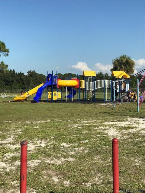 A colorful playground structure stands on a grassy field under a clear blue sky — 470 N Cabbage Palm St, Clewiston FL 33440, CLEWISTON, FL