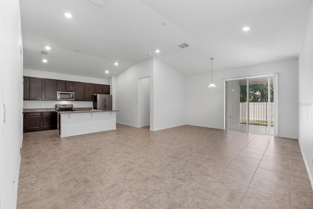 An open-concept kitchen and living area features dark wood cabinets, granite countertops, and tile flooring — 7608 SUNSHINE BRIDGE AVENUE, GIBSONTON, FL