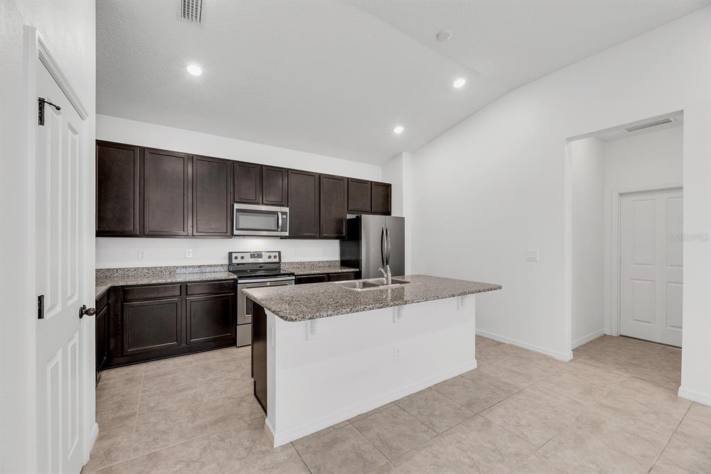 A kitchen features dark wood cabinets, granite countertops, a central island, and stainless steel appliances — 7608 SUNSHINE BRIDGE AVENUE, GIBSONTON, FL