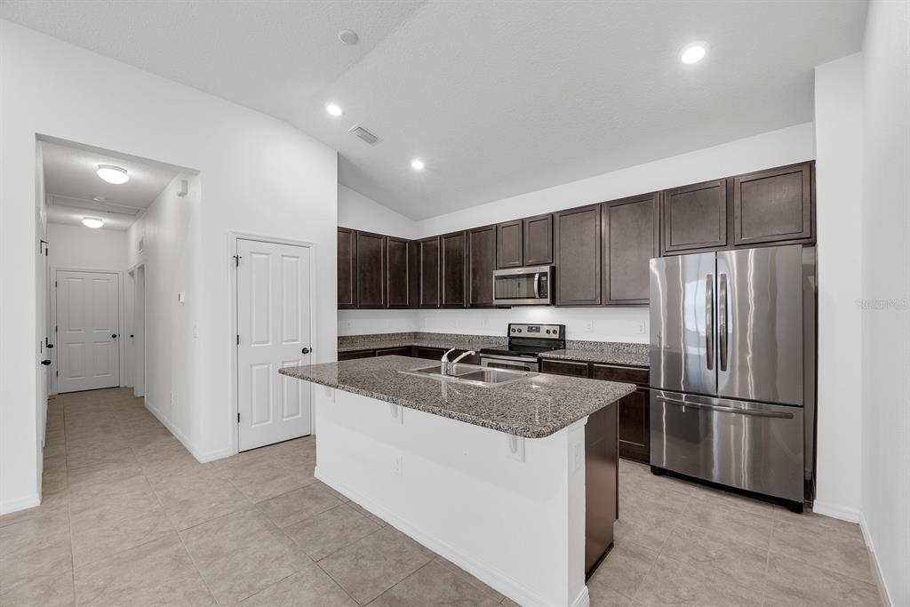 A kitchen features dark wood cabinets, granite countertops, a kitchen island, and stainless steel appliances — 7608 SUNSHINE BRIDGE AVENUE, GIBSONTON, FL