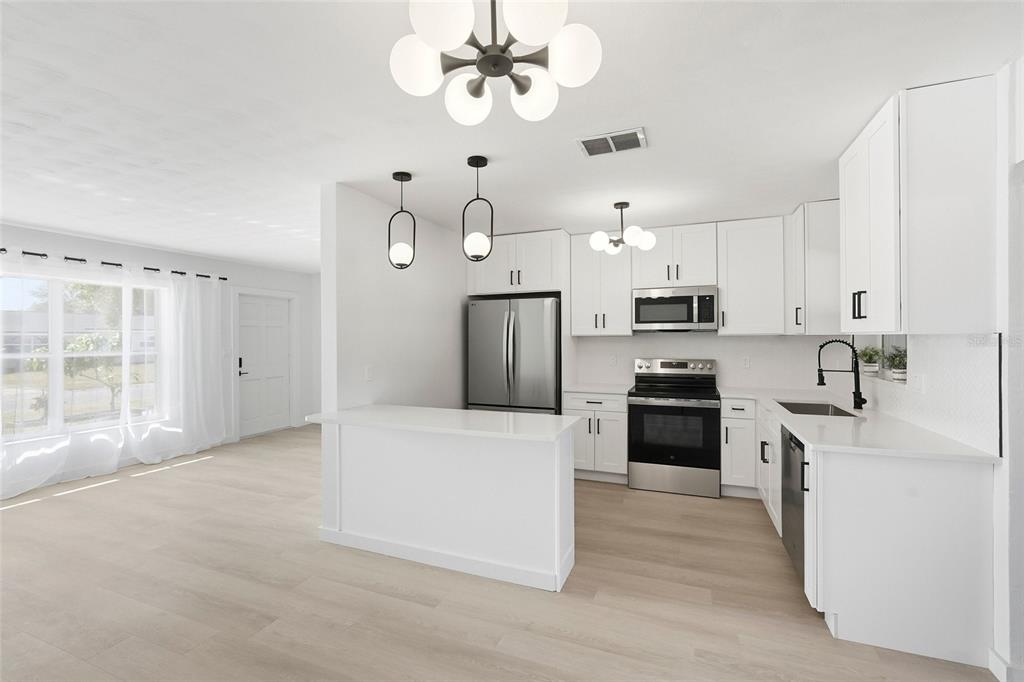 A bright, open-concept kitchen features white cabinetry, stainless steel appliances, and light wood flooring — 2845 64TH TERRACE S, ST PETERSBURG, FL