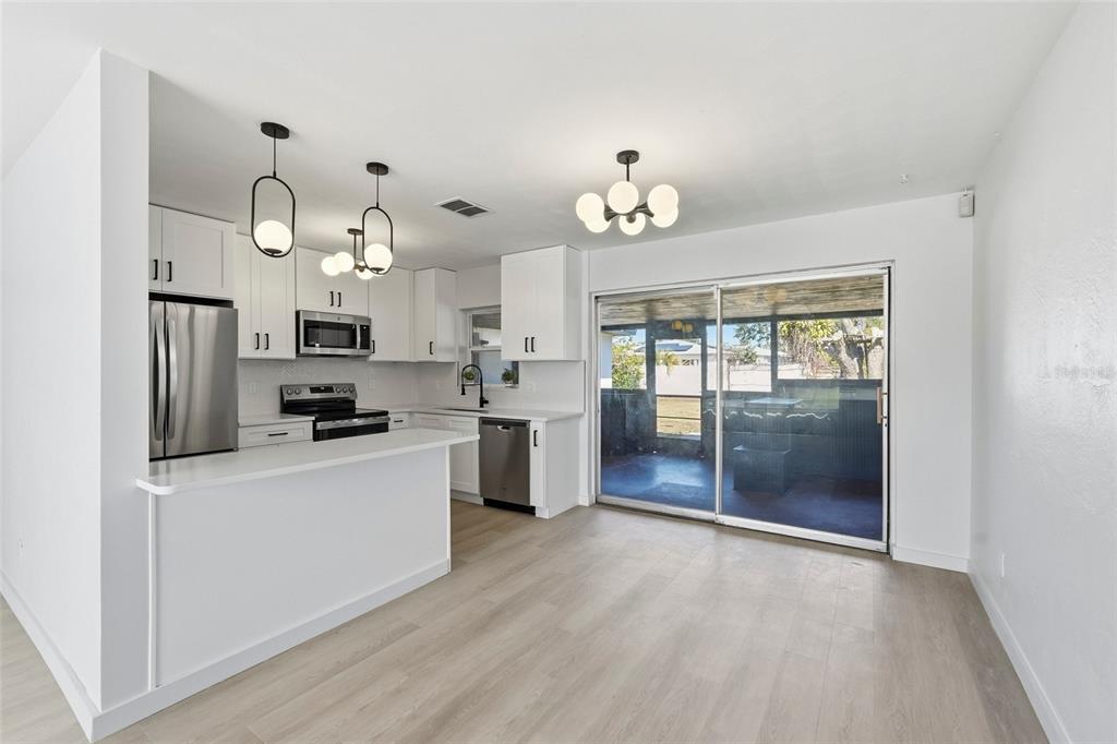 A modern kitchen features white cabinetry, stainless steel appliances, and a sliding glass door — 2845 64TH TERRACE S, ST PETERSBURG, FL
