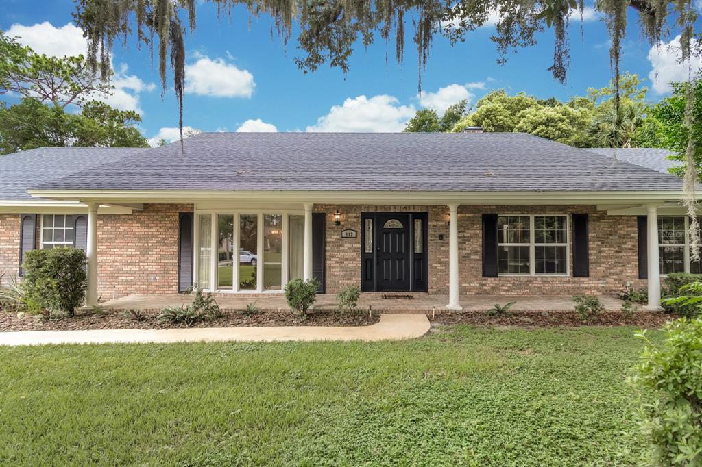 A single-story brick house with a covered front porch, black shutters, and a dark door — 112 FOREST PARK COURT, LONGWOOD, FL