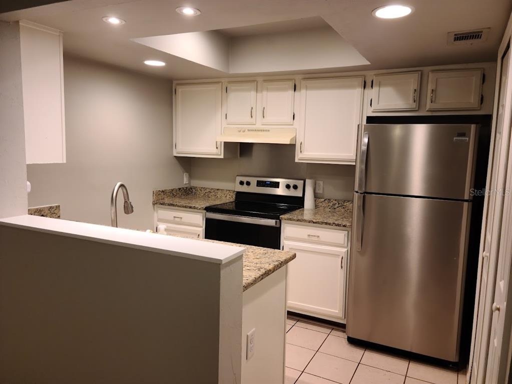 A kitchen features white cabinets, granite countertops, stainless steel appliances, and tile flooring — 900 SW 62ND BOULEVARD UNIT B 8, GAINESVILLE, FL