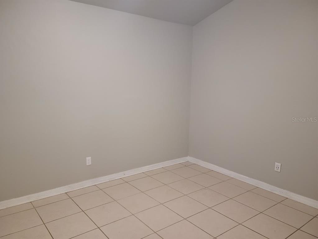 An empty room with light gray walls, white baseboards, and light-colored square floor tiles — 900 SW 62ND BOULEVARD UNIT B 8, GAINESVILLE, FL