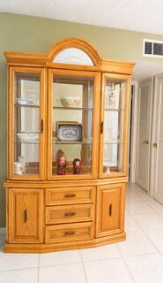 A wooden china cabinet with glass doors and drawers stands against a light green wall — 175 Flanders D, Delray Beach FL 33484, DELRAY BEACH, FL