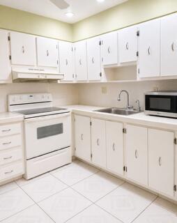 A kitchen with white cabinets, white appliances, a stainless steel sink, and light-colored tile floors — 175 Flanders D, Delray Beach FL 33484, DELRAY BEACH, FL