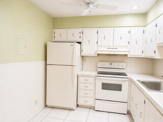 A kitchen features white appliances, white cabinets, light green walls, and white floor tiles — 175 Flanders D, Delray Beach FL 33484, DELRAY BEACH, FL