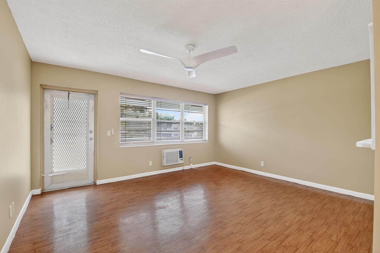 An empty room features tan walls, wood-look flooring, a ceiling fan, and a window unit — 265 Windsor # L, West Palm Beach FL 33417, WEST PALM BEACH, FL