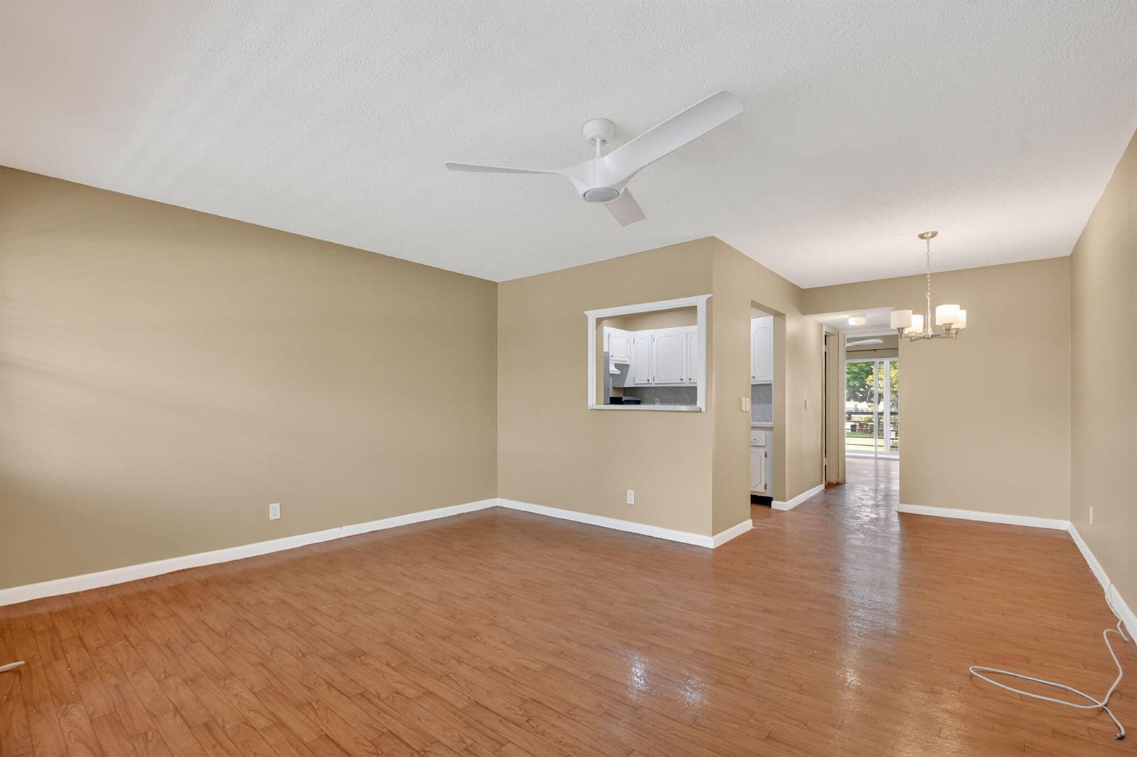 An empty living room features tan walls, wood-look flooring, a ceiling fan, and a pass-through window — 265 Windsor # L, West Palm Beach FL 33417, WEST PALM BEACH, FL