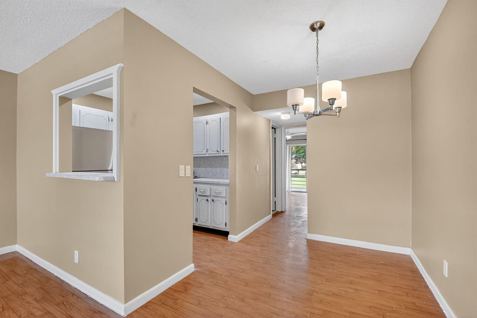A dining area with wood-look flooring leads to a kitchen and a hallway with exterior views — 265 Windsor # L, West Palm Beach FL 33417, WEST PALM BEACH, FL