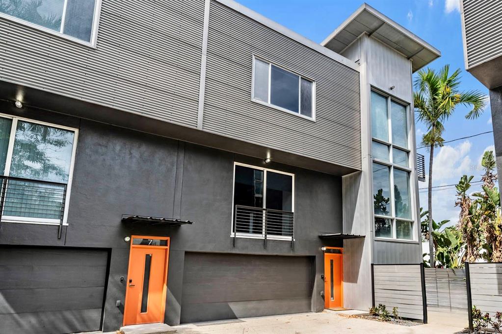 A modern multi-story townhouse exterior features corrugated metal siding, dark gray walls, and orange doors — 3107 W DE LEON STREET UNIT 6, TAMPA, FL