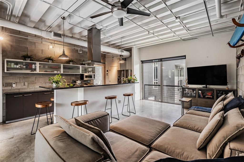An open-concept living area features a kitchen with bar seating, concrete floors, and industrial ceilings — 3107 W DE LEON STREET UNIT 6, TAMPA, FL