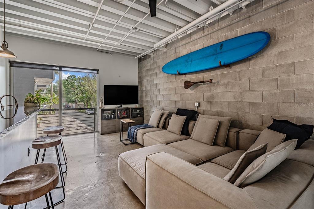 A living room features a concrete block wall, a blue surfboard, and a large sectional sofa — 3107 W DE LEON STREET UNIT 6, TAMPA, FL