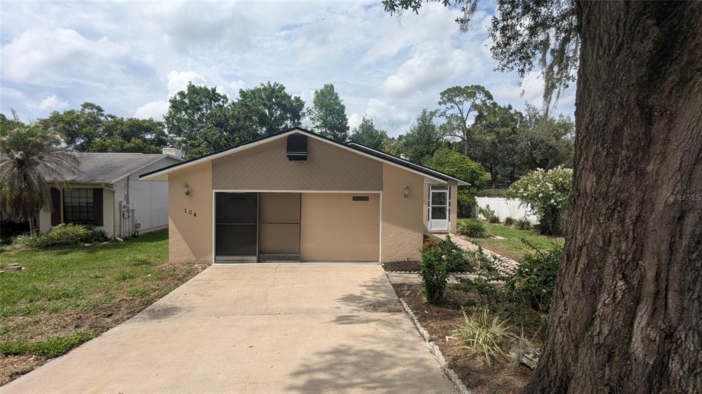 A single-story house with a beige stucco exterior, a concrete driveway, and a large tree — 104 QUAIL RIDGE COURT, SANFORD, FL
