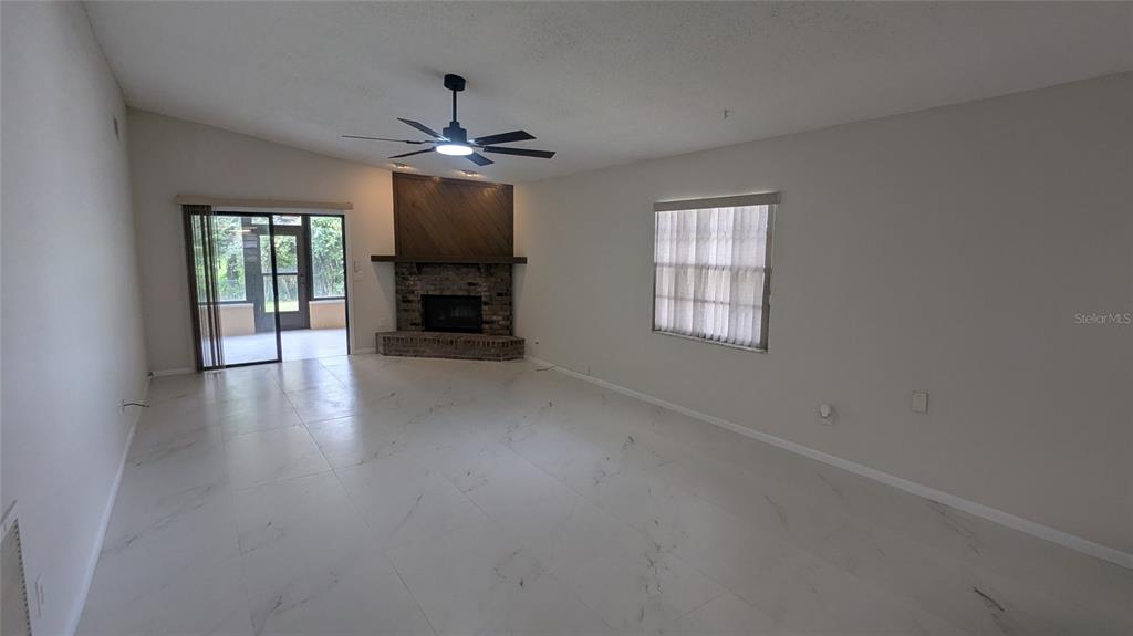A living room with white tile floors, a corner brick fireplace, and a sliding glass door — 104 QUAIL RIDGE COURT, SANFORD, FL