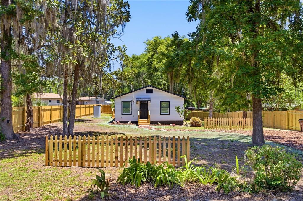 A white house with a dark roof sits in a yard enclosed by wooden fencing — 816 WOODLAND AVENUE, LEESBURG, FL