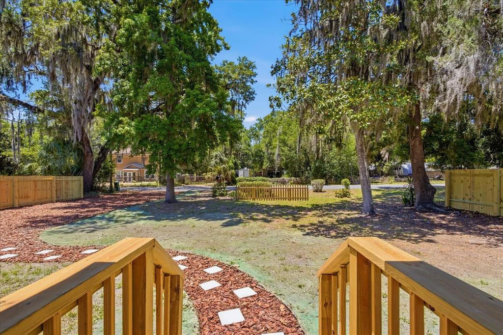 A wooden deck overlooks a backyard with a stone path, mulch, and mature trees — 816 WOODLAND AVENUE, LEESBURG, FL