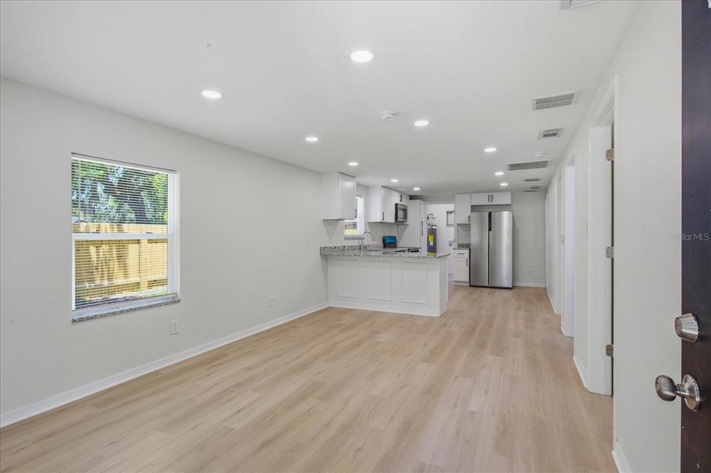 A bright, open-concept kitchen and living area featuring light wood-look flooring and recessed lighting — 816 WOODLAND AVENUE, LEESBURG, FL