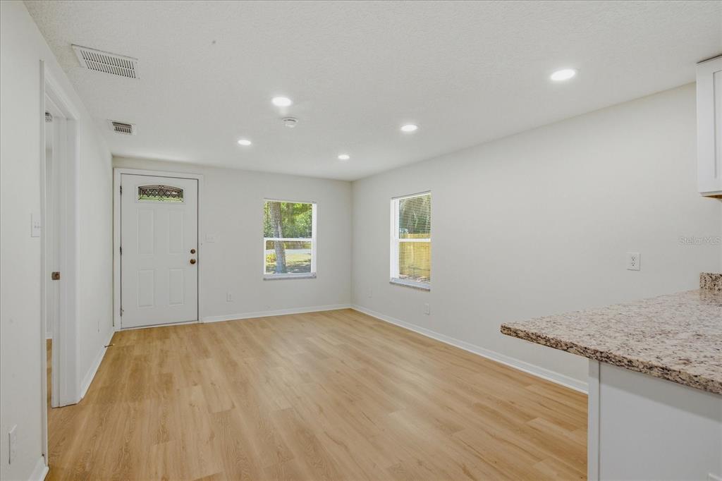 A bright living area features light wood-look flooring, white walls, recessed lighting, and two windows — 816 WOODLAND AVENUE, LEESBURG, FL